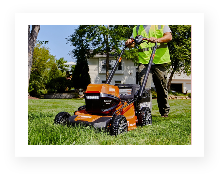 A man in an orange shirt is cutting grass with a lawn mower.