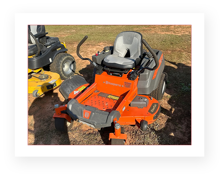 A lawn mower sitting in the dirt next to other vehicles.