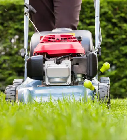 A person is standing on the grass while using a lawn mower.